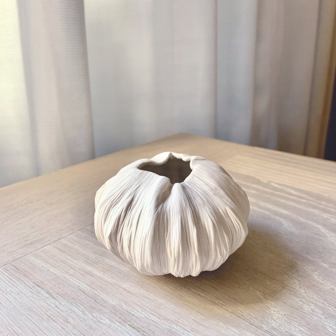 Roundish porcelain pinch pot vase. The vase is shaped and altered from a ball of porcelain clay. It's carved with fine carving tool around the entire vase. The vase has uneven/altered rim.